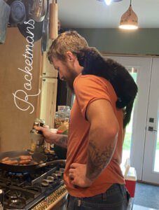 Rocket sitting on Rocketmans Owners shoulder watching him cook